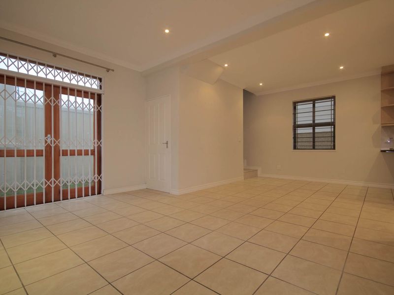 An open-plan living area featuring neutral tiled flooring, recessed lighting, and direct access to the exterior through a secure wooden door.