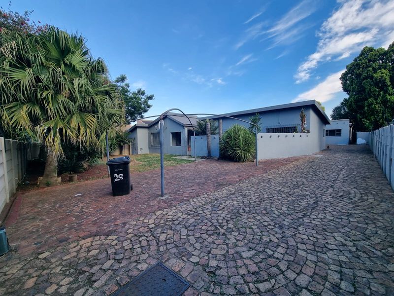 Front exterior view of the property featuring a cobblestone driveway, metal carport structure, and perimeter walling with security bars on windows.