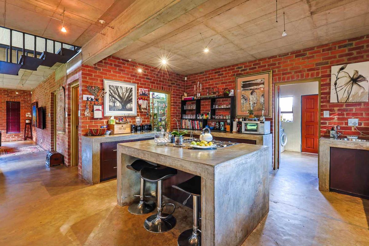 Industrial-style kitchen featuring exposed brick walls, concrete island with integrated cooktop, polished concrete flooring, and an open-plan layout.