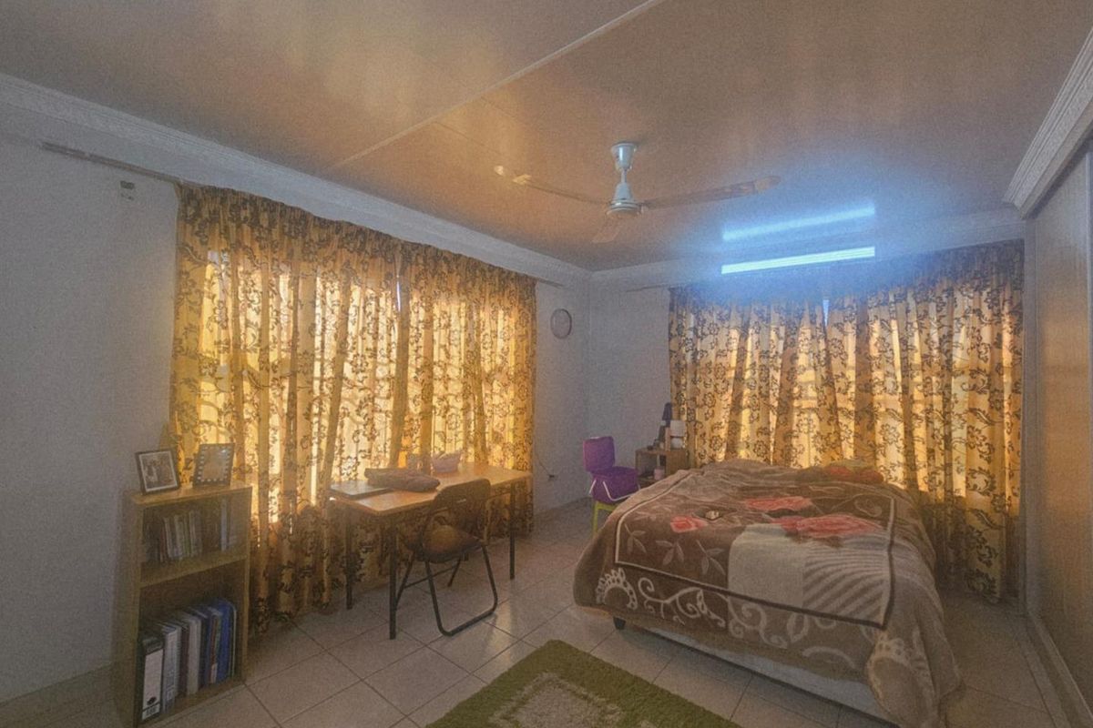 A spacious bedroom featuring tiled flooring, a ceiling fan, and large windows covered by patterned curtains, providing ample natural light.