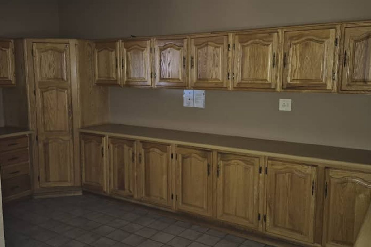 A functional kitchen area featuring extensive wooden cabinetry, tiled flooring, and ample counter space, offering a traditional aesthetic with practical storage solutions.