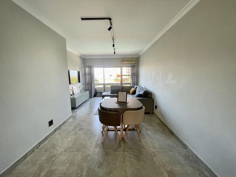 Open-plan living and dining area featuring large format floor tiles, modern track lighting, and a sliding glass door leading to an outdoor space.