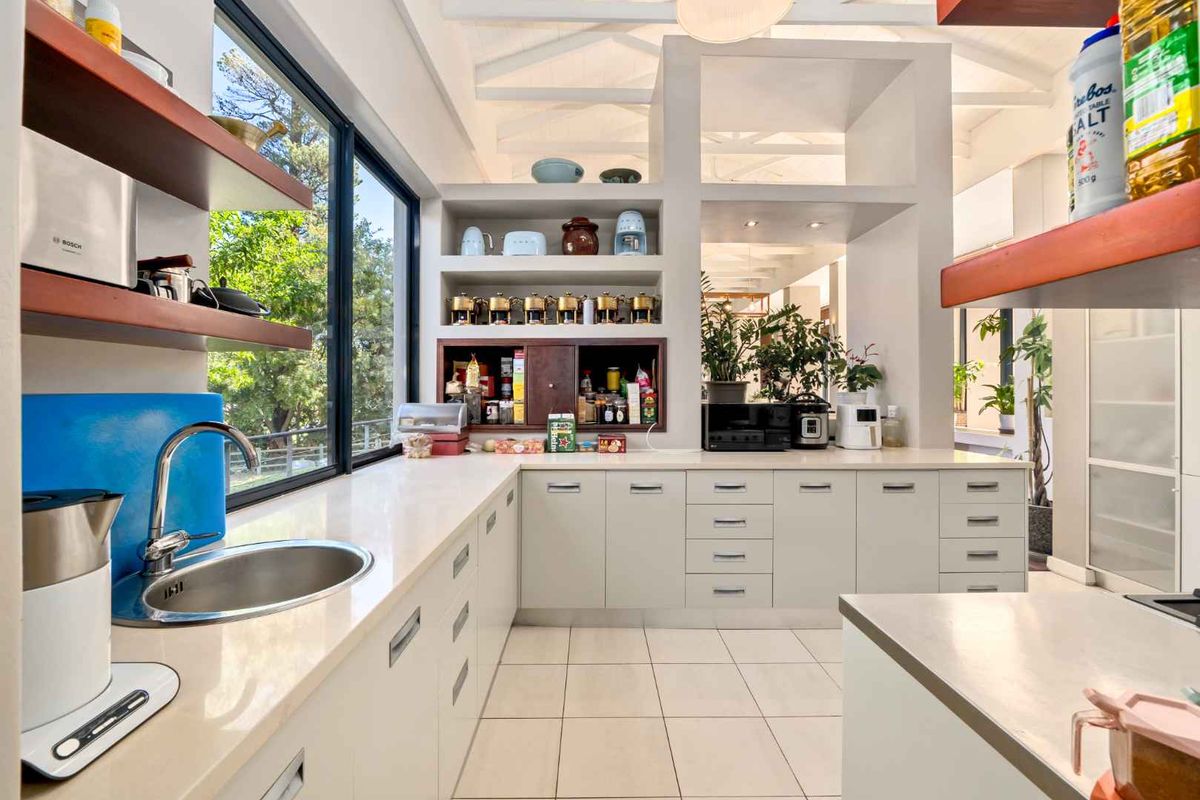 Modern kitchen featuring white cabinetry, stone countertops, integrated sink, and large windows providing natural light and garden views.