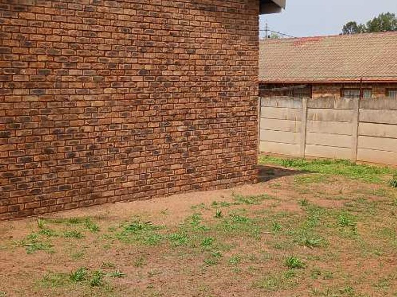 Rear exterior view of the property featuring a face brick facade and a precast concrete boundary wall with an undeveloped garden area.