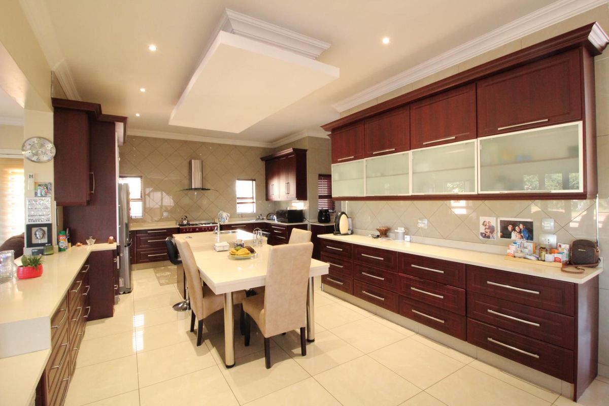 Spacious kitchen featuring dark wood cabinetry, stone countertops, a central island with integrated seating, and tiled flooring with recessed ceiling lighting.