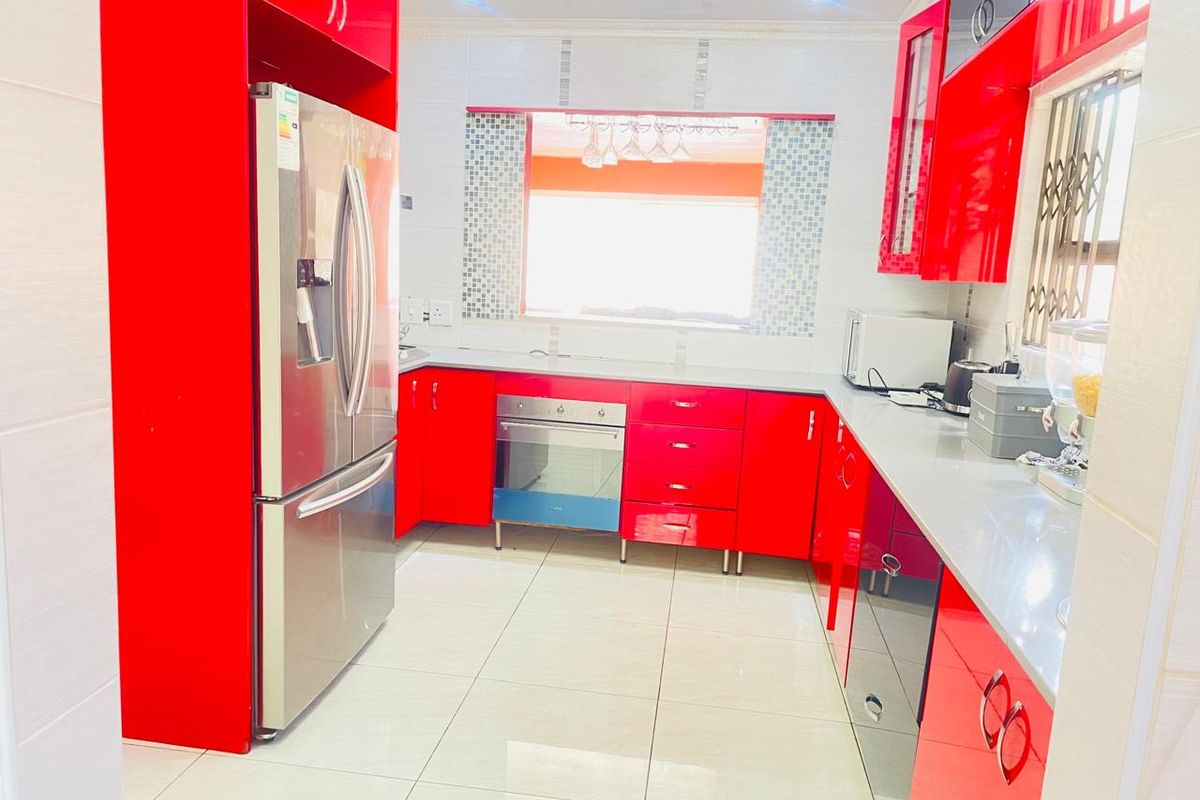 A modern kitchen featuring high-gloss red cabinetry, stone countertops, tiled flooring, and built-in oven, offering a vibrant and functional culinary space.