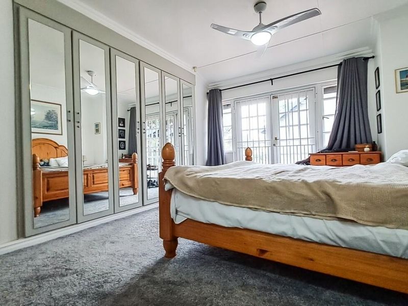 Spacious bedroom featuring extensive built-in mirrored wardrobes, a ceiling fan, and direct access to an outdoor area through classic french doors.