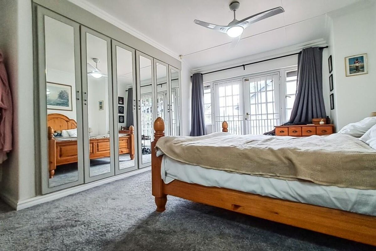 Spacious bedroom featuring extensive built-in mirrored wardrobes, a ceiling fan, and direct access to an outdoor area through classic french doors.