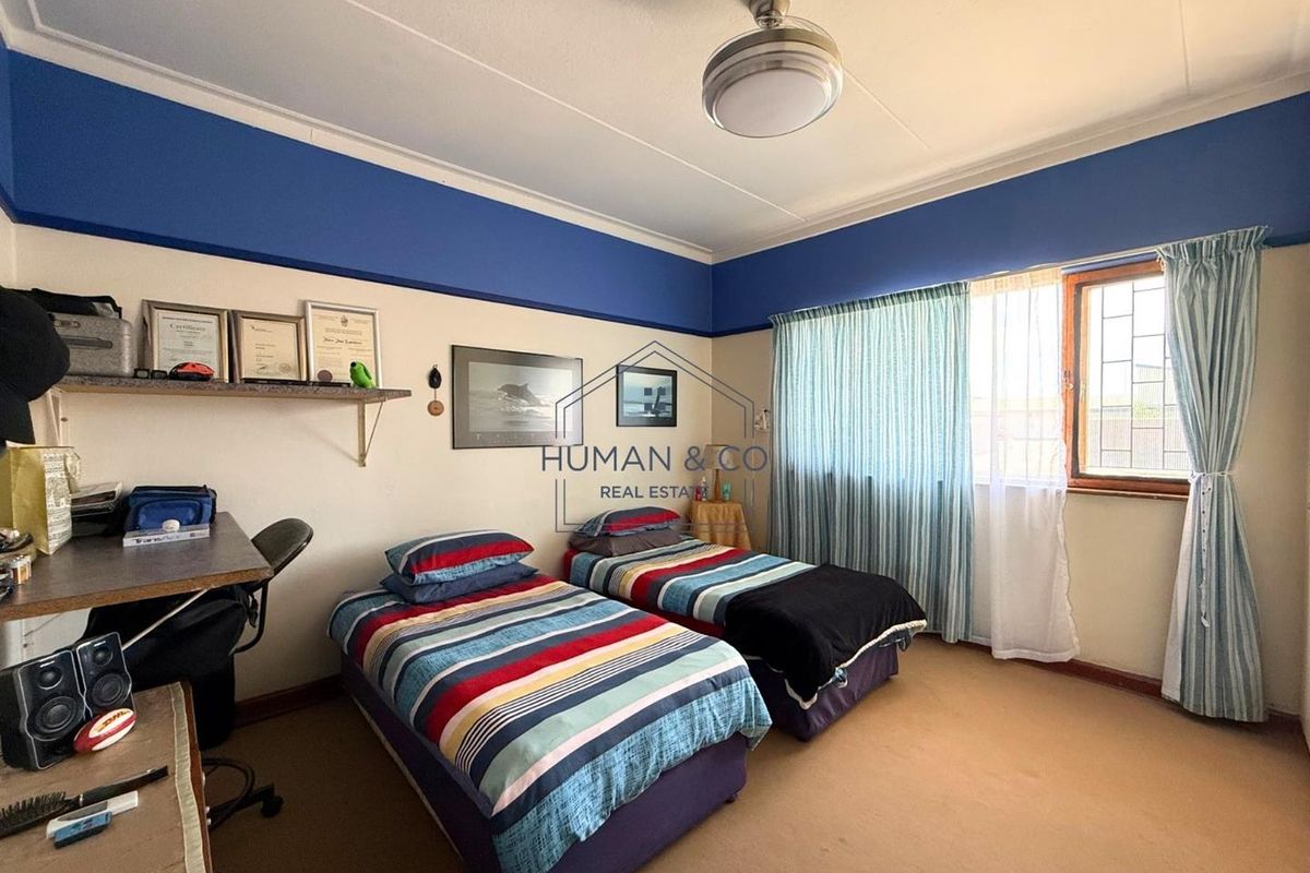 A bedroom featuring carpeted flooring, a ceiling fan, and a window with security bars, offering a functional space for rest or study.