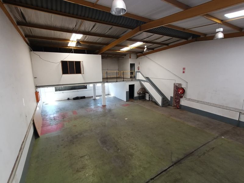 Spacious industrial warehouse unit featuring a mezzanine level, exposed steel roof trusses, concrete flooring, and integrated fire safety equipment.
