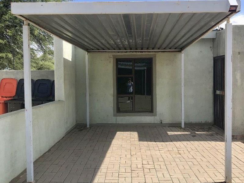 A functional outdoor carport area featuring a metal roof structure and paved flooring, providing covered parking space for the property.