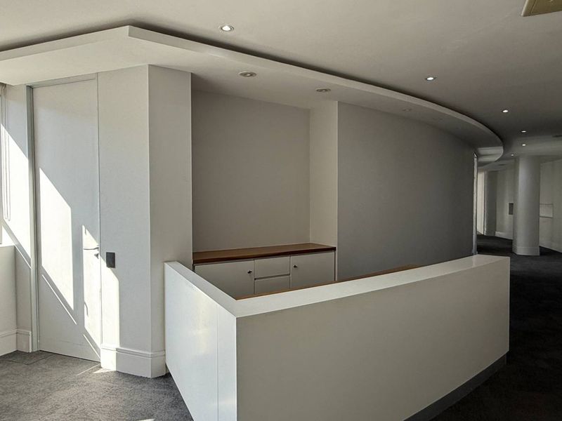 A modern, empty office space featuring a built-in reception desk, curved architectural wall, and recessed ceiling lighting with neutral finishes.