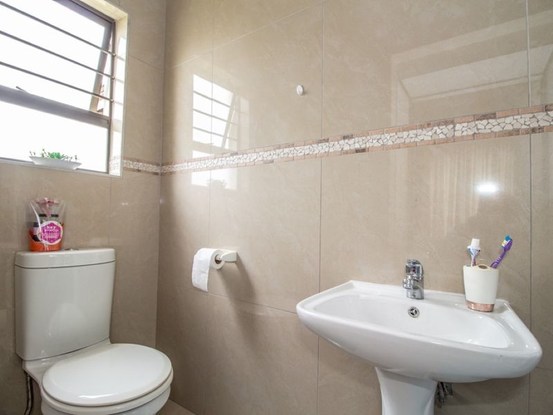 A clean and well-maintained bathroom featuring neutral ceramic wall tiles with a decorative mosaic border, a pedestal washbasin, and a standard toilet.
