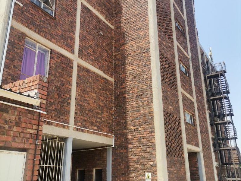 Exterior view of a multi-story apartment building featuring exposed brickwork, concrete structural framing, and an external metal fire escape staircase.