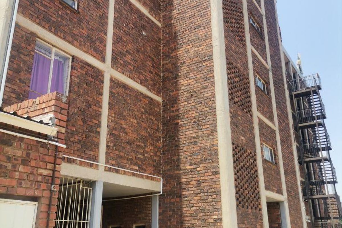 Exterior view of a multi-story apartment building featuring exposed brickwork, concrete structural framing, and an external metal fire escape staircase.