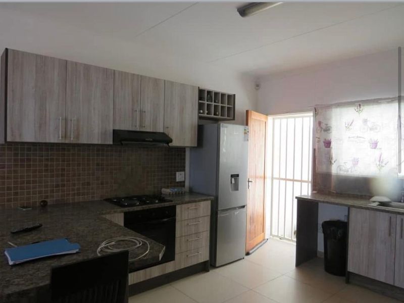 Functional kitchen featuring laminate cabinetry, granite countertops, mosaic tile backsplash, built-in oven, gas hob, and direct access to an exterior security gate.