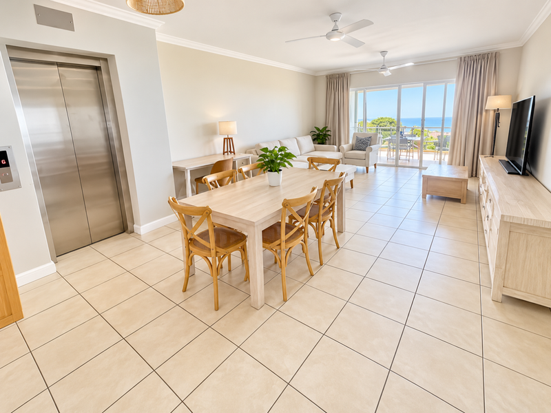 Spacious open-plan living and dining area featuring tiled floors, ceiling fans, and direct access to a balcony with ocean views via sliding glass doors.