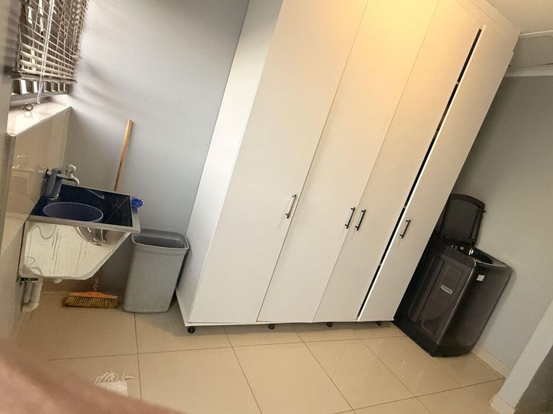 A functional laundry room featuring tiled flooring, a utility sink, and ample built-in storage cabinetry.