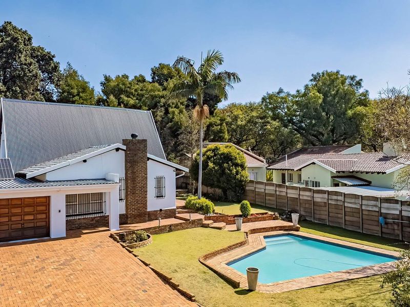 Aerial view of the rear property featuring a swimming pool, brick paved driveway, garage, and solar panels set within a landscaped garden.