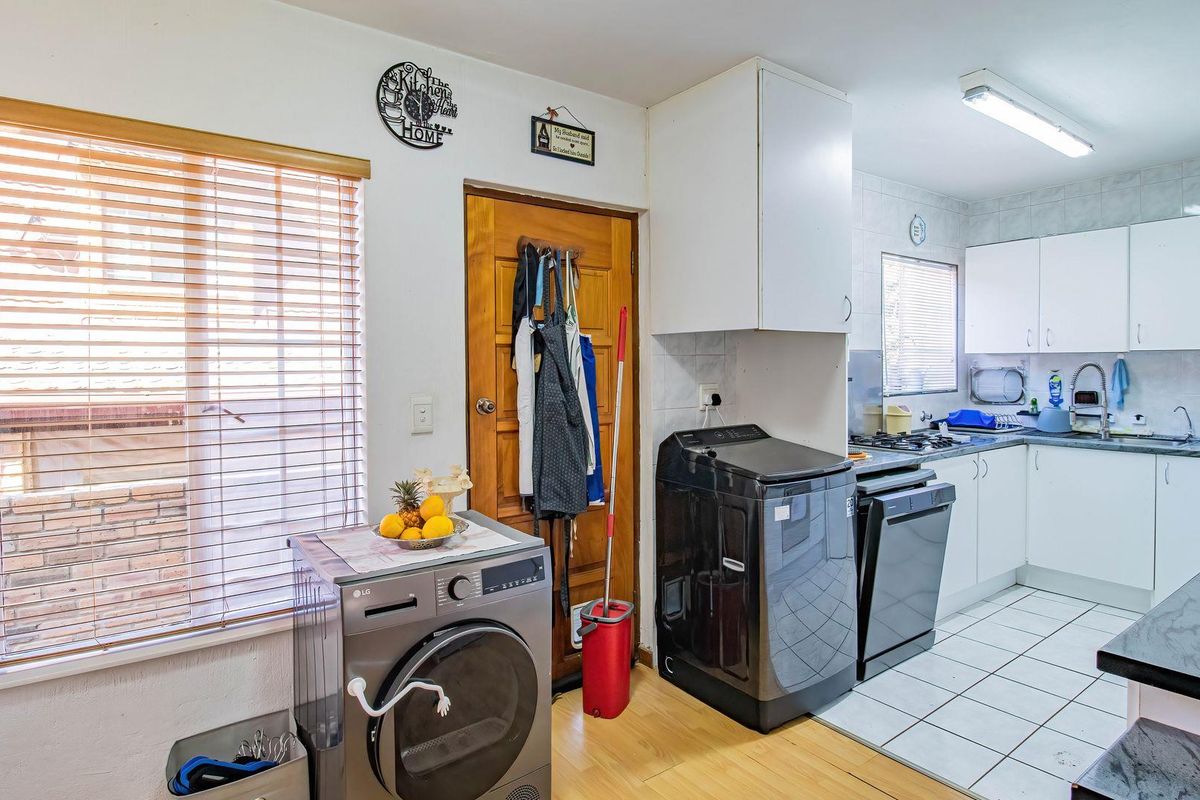 Functional kitchen area featuring built-in cabinetry, tiled and laminate flooring, and integrated cooking appliances, with a dedicated laundry space adjacent to the main kitchen.