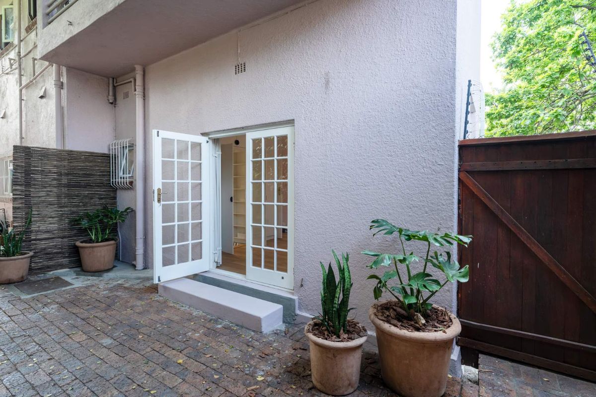 A private rear courtyard featuring brick paving, a timber gate, and classic white french doors providing access to the interior living space.