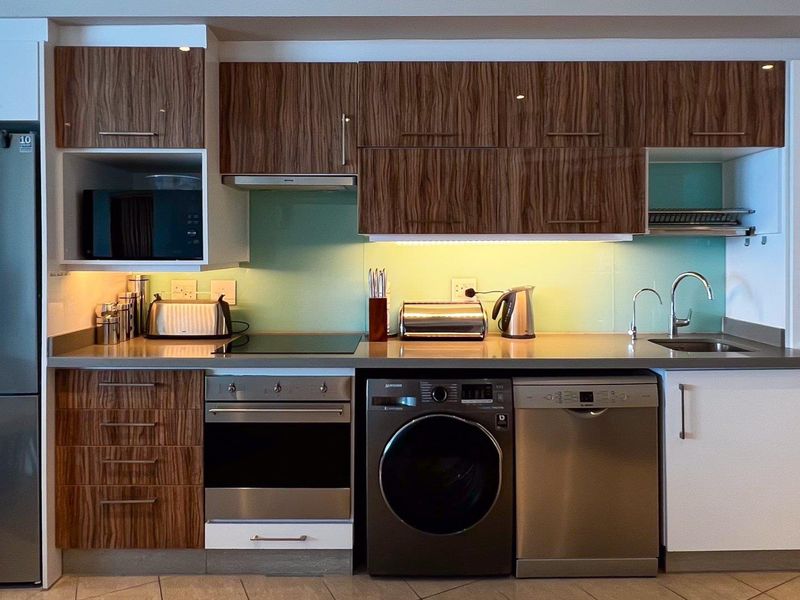 Modern kitchen featuring wood-grain cabinetry, stone countertops, glass splashback, and integrated appliances including an oven, hob, and extractor fan.