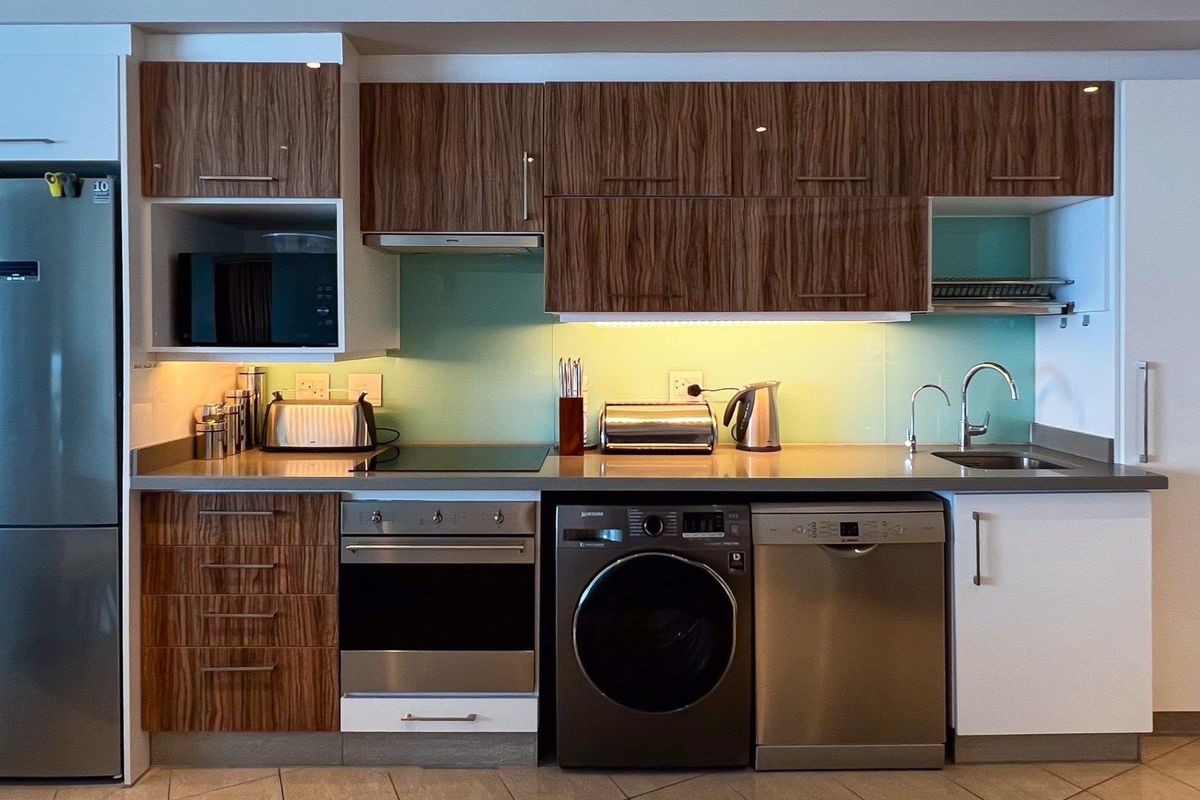 Modern kitchen featuring wood-grain cabinetry, stone countertops, glass splashback, and integrated appliances including an oven, hob, and extractor fan.