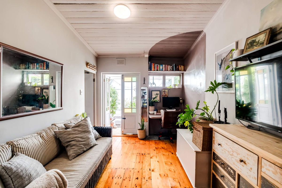 A cozy living area featuring polished timber flooring, a unique timber-paneled ceiling, and a built-in study nook leading to an outdoor space.