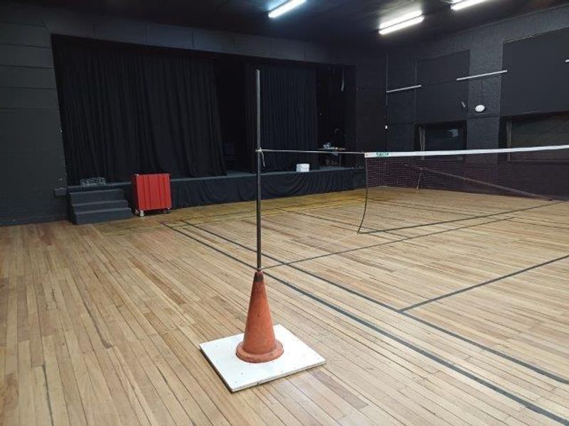 A multi-purpose sports facility featuring a hardwood floor, a raised stage area with curtains, and functional overhead lighting.