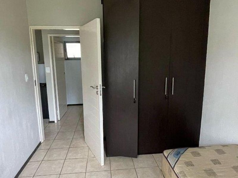 A bedroom featuring tiled flooring and a dark wood built-in wardrobe, with an open doorway leading to an adjacent hallway.