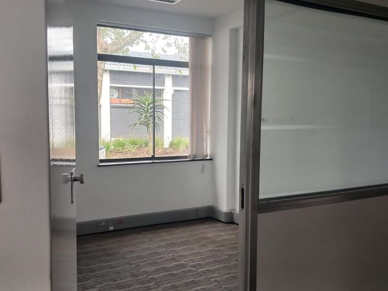 A vacant office space featuring carpet flooring, a frosted glass partition, and a window providing natural light.