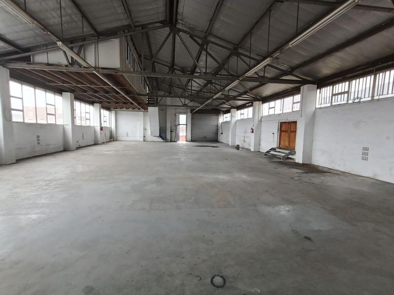 Spacious industrial warehouse unit featuring high ceilings with exposed steel trusses, concrete flooring, and large windows providing ample natural light.
