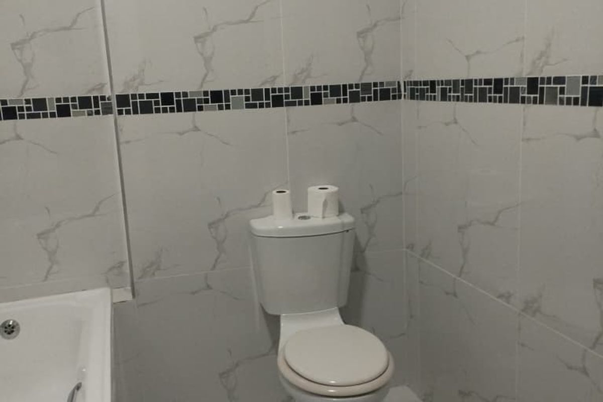 A clean, modern bathroom featuring white marble-effect wall tiles with a decorative mosaic border, a white toilet, and a built-in bathtub.