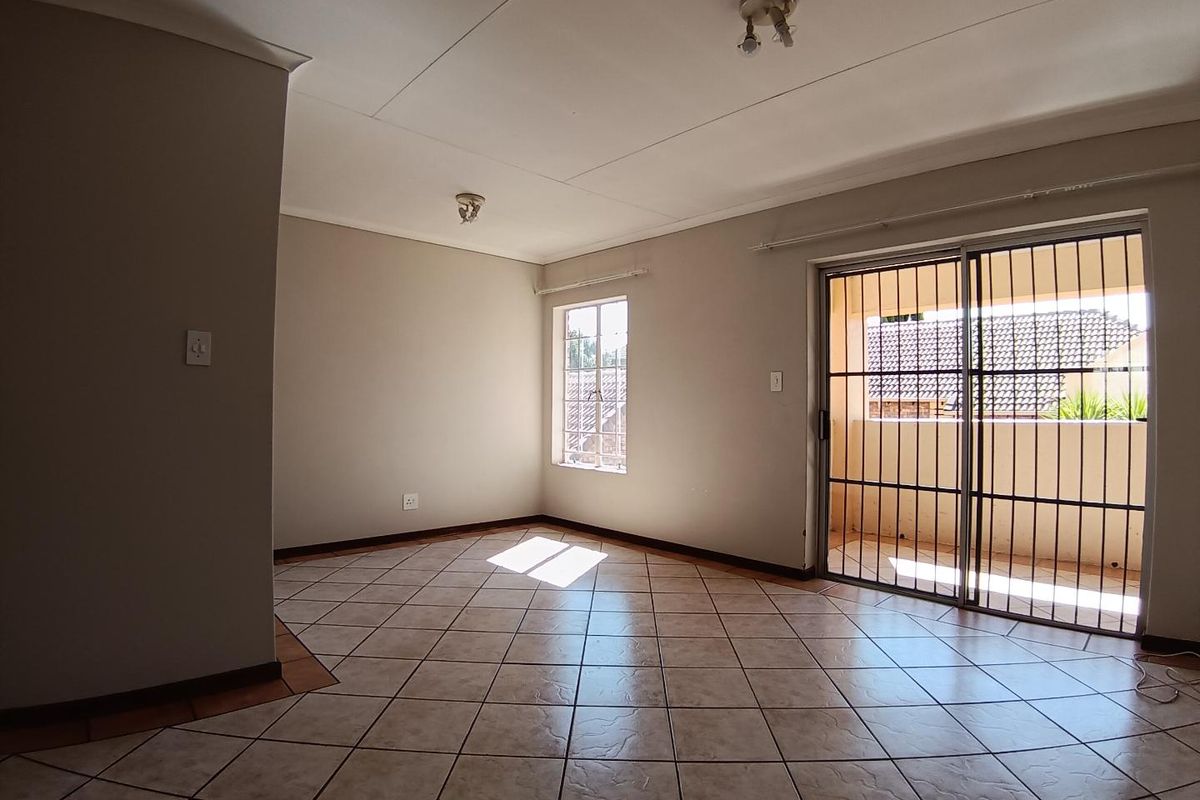 A bright, empty living room featuring neutral tiled flooring, natural light from a window, and a sliding glass door leading to an outdoor area.