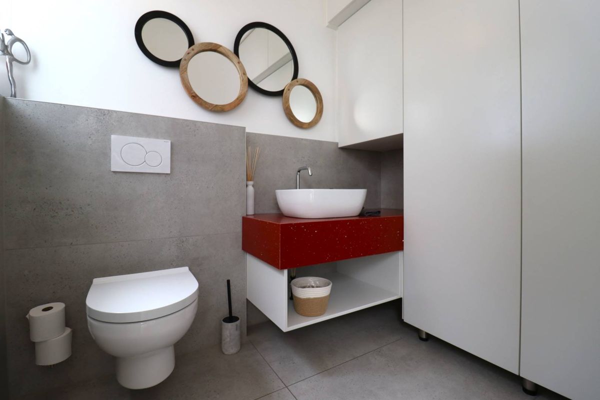 Modern bathroom featuring a wall-hung toilet with concealed cistern, a vessel sink on a red vanity unit, and neutral grey floor and wall tiling.