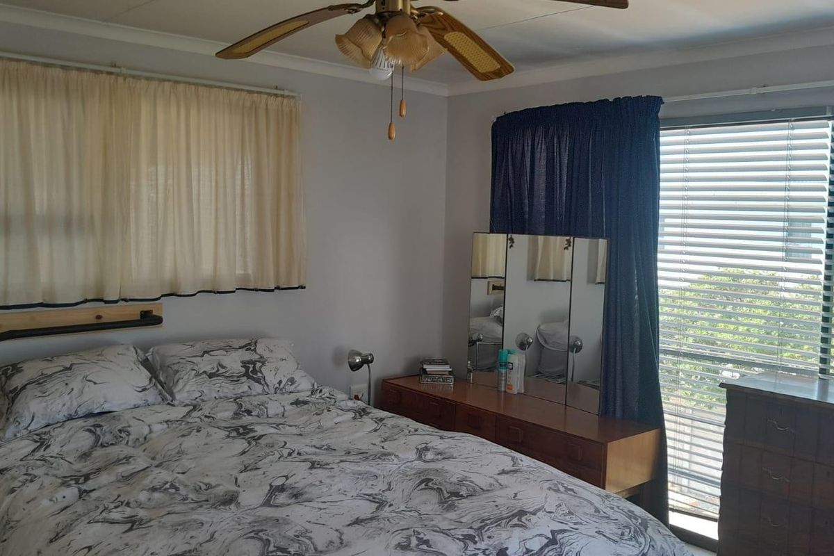A bedroom featuring a ceiling fan, large windows with blinds, and neutral wall finishes.