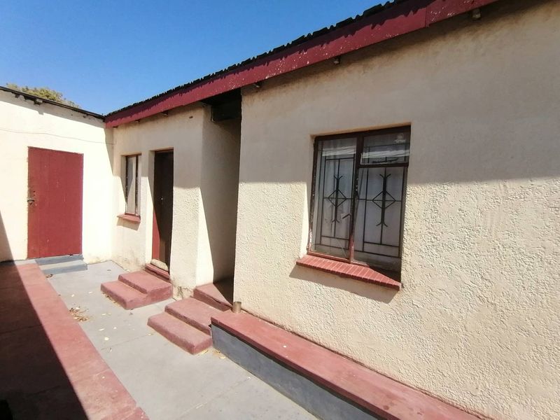 Rear exterior view of the property featuring plastered walls, security bars on windows, and concrete access steps.