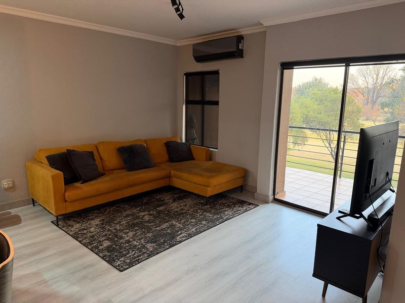 A bright living room featuring modern laminate flooring, a wall-mounted air conditioning unit, and large sliding glass doors leading to an outdoor balcony.