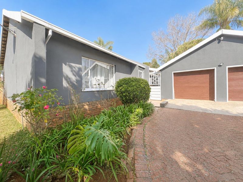 Front exterior view of the house featuring a brick driveway, well-maintained garden beds, and a double garage with roller doors.