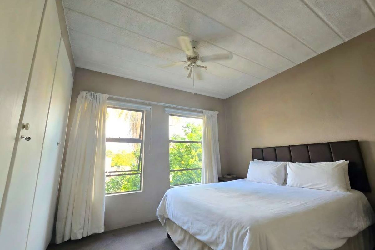 A functional bedroom featuring built-in cupboards, a ceiling fan, and natural light through two windows.