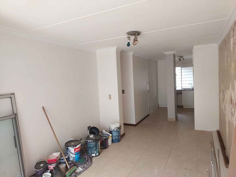 An open-plan living and kitchen area currently undergoing renovation, featuring tiled floors and visible wall surface repairs.