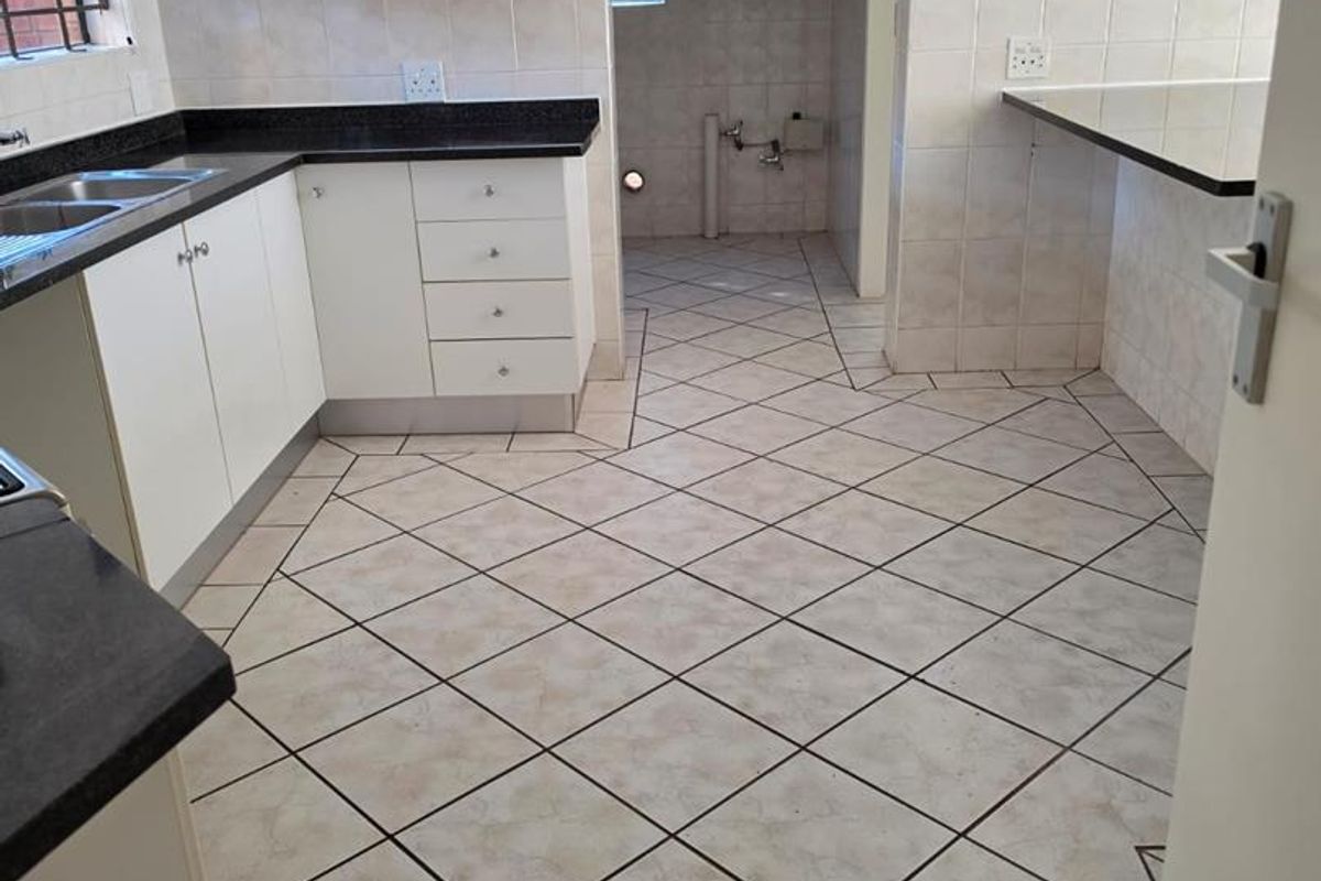 A functional, empty kitchen featuring white cabinetry, dark countertops, tiled flooring, and a breakfast bar, with an adjacent utility area.