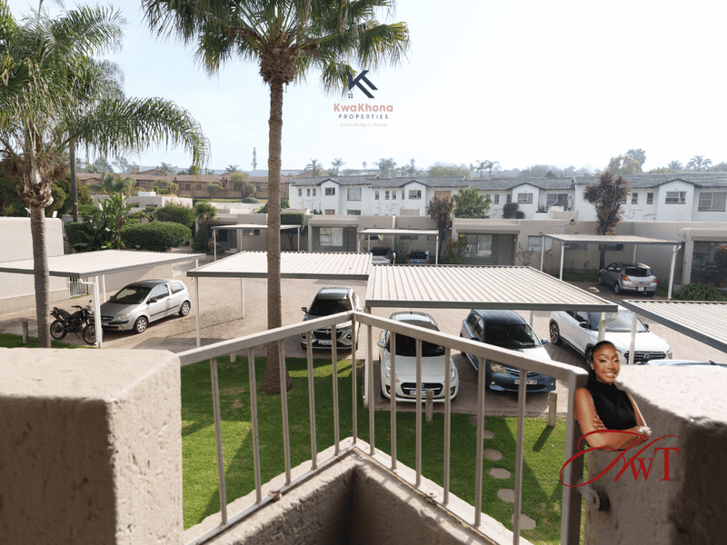 Elevated view overlooking a townhouse complex courtyard featuring paved parking areas, carports, and established garden landscaping.