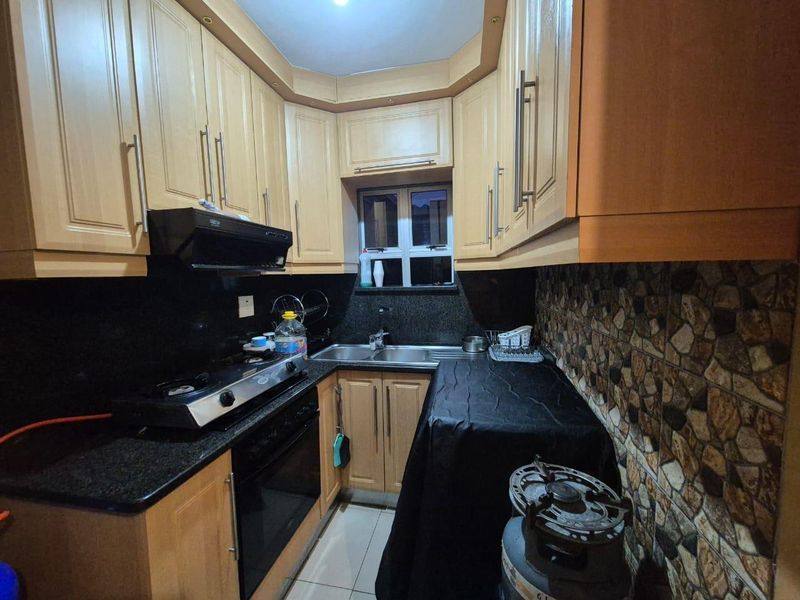 Compact kitchen featuring light wood cabinetry, granite countertops, a stainless steel double sink, and built-in cooking appliances with a decorative tiled backsplash.
