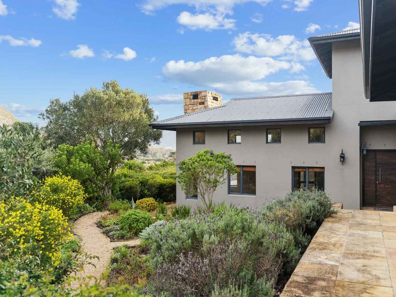 A well-maintained rear exterior view featuring a stone chimney, corrugated metal roof, and a beautifully landscaped garden with a stone paved walkway.