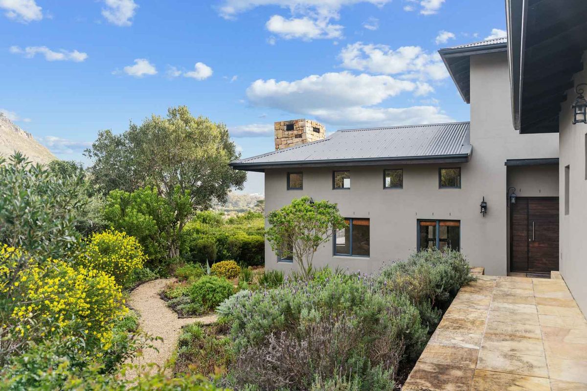 A well-maintained rear exterior view featuring a stone chimney, corrugated metal roof, and a beautifully landscaped garden with a stone paved walkway.