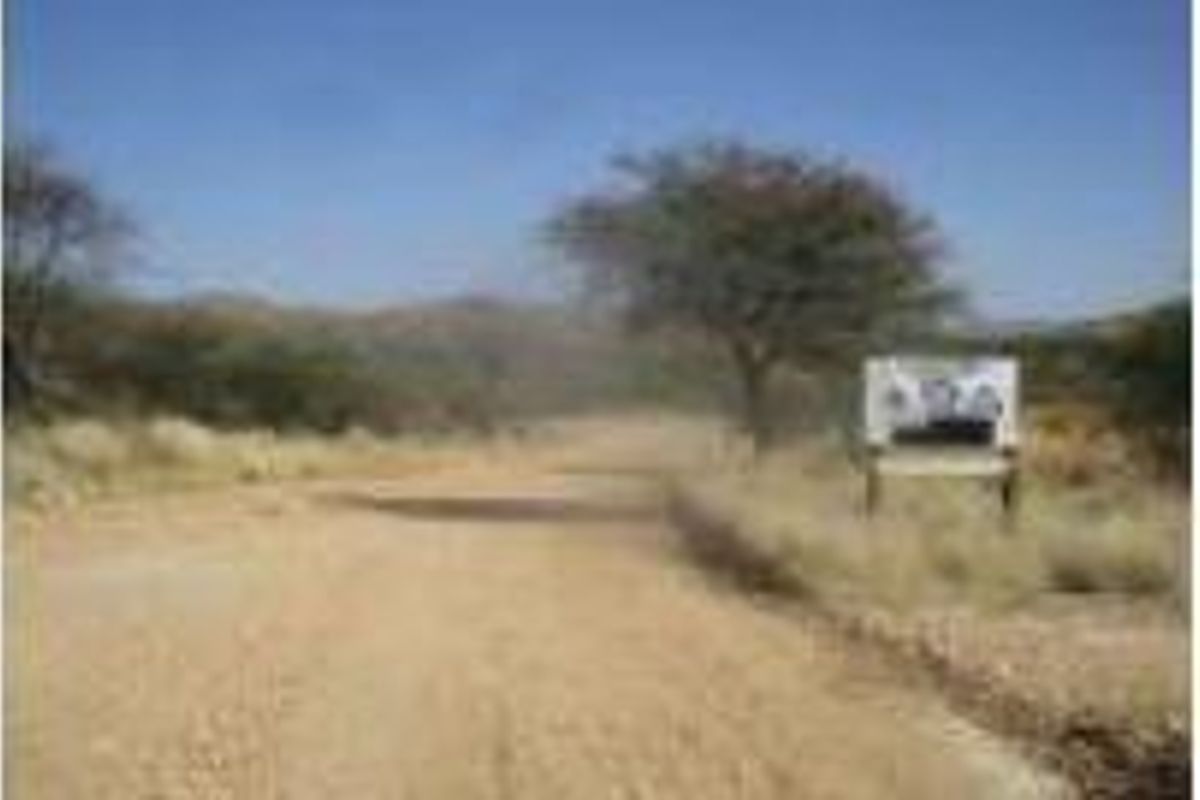 A view of a rural dirt road leading towards a landscape with trees and hills, featuring a roadside sign.