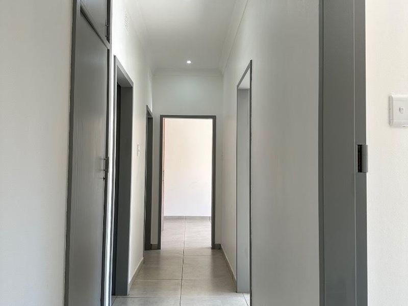 A clean, modern hallway featuring neutral tiled flooring, recessed downlighting, and a built-in storage cupboard.