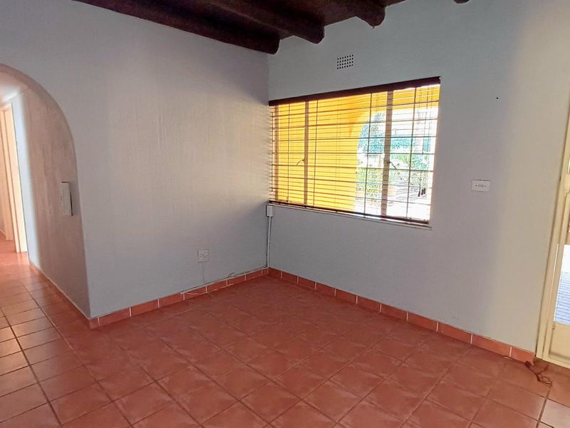 An empty living area featuring exposed timber ceiling beams, ceramic floor tiles, and an arched entryway leading to a hallway.