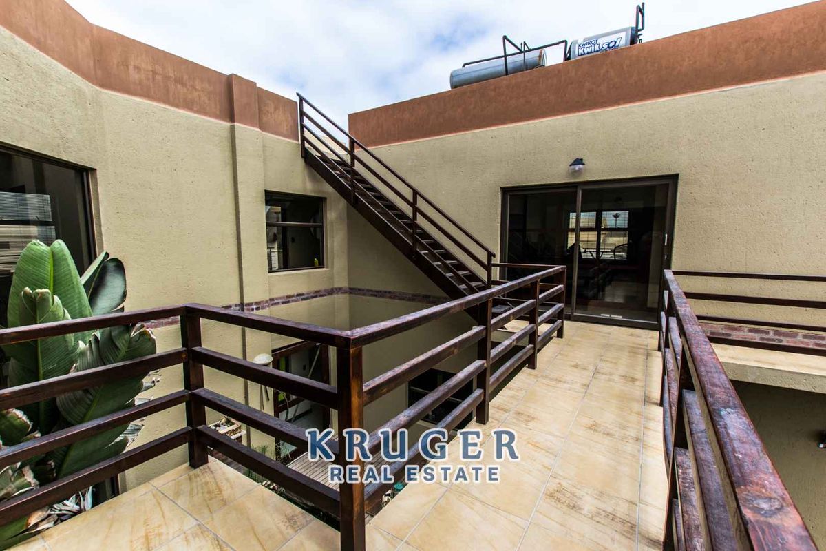 An exterior view of a multi-level courtyard featuring a wooden staircase, tiled balcony walkway, and a solar water heating system on the roof.